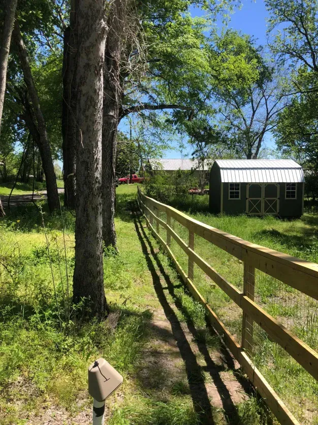 A wooden fence surrounds a grassy field with a shed in the background.