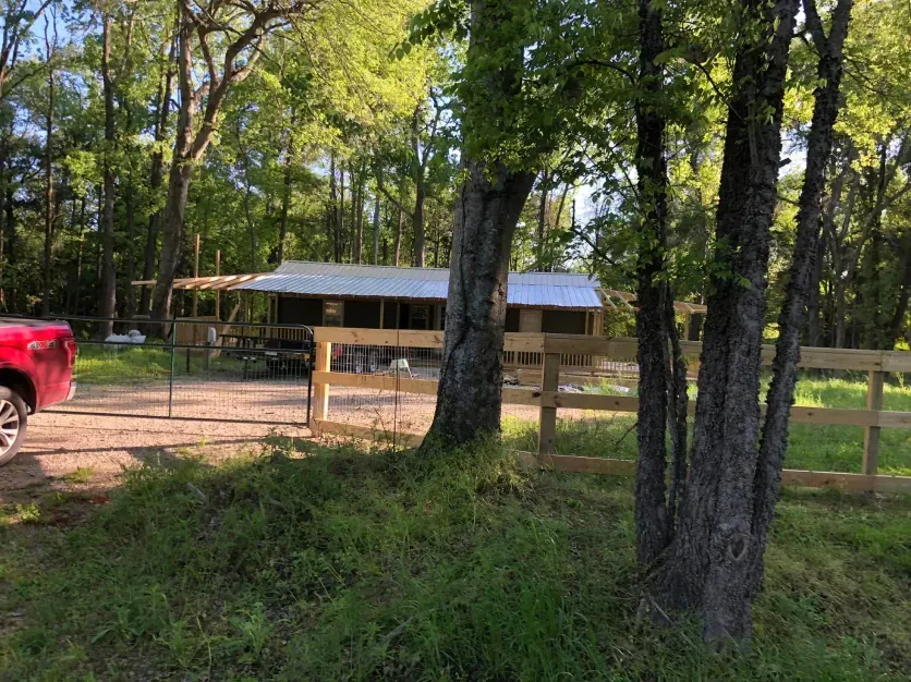 A red truck is parked in front of a house in the woods.