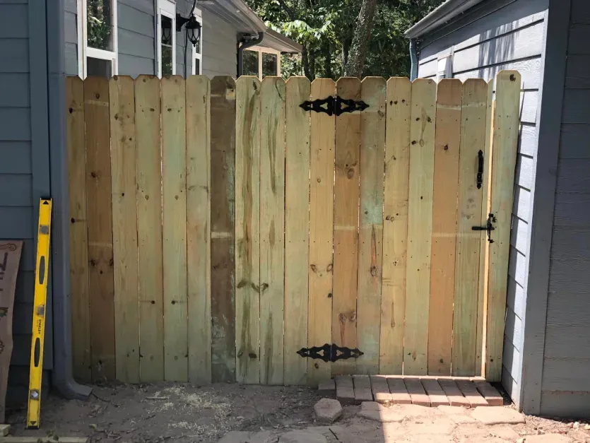 A wooden fence with a gate is being built in front of a house.