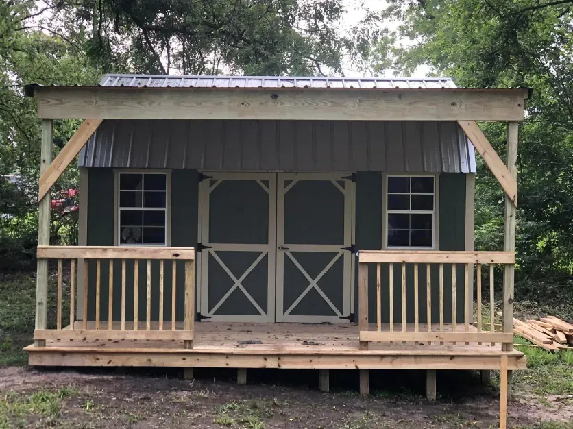 A green shed with a porch and a wooden deck.