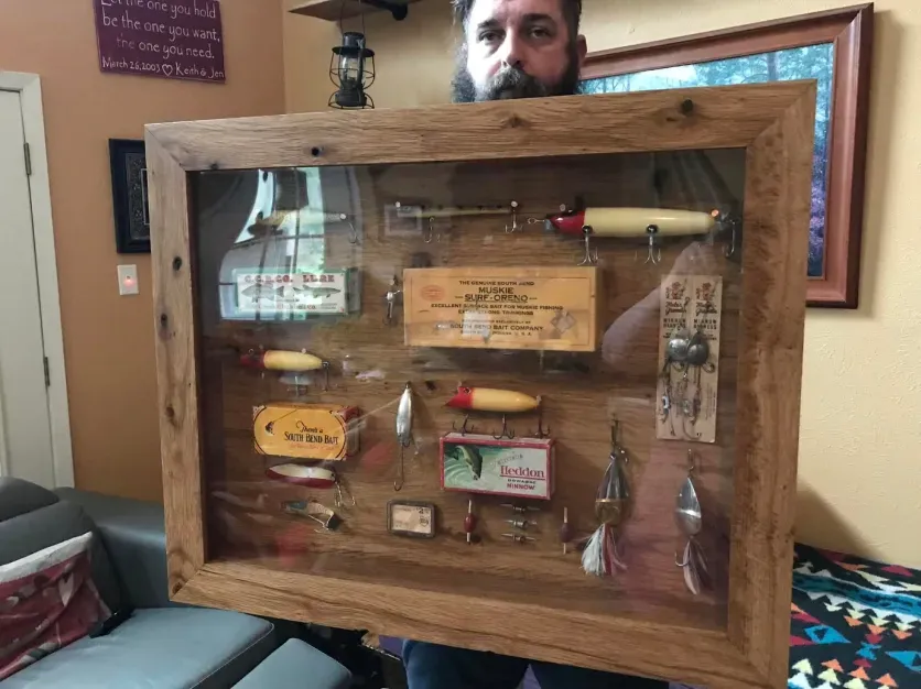 A man is holding a framed display of fishing lures