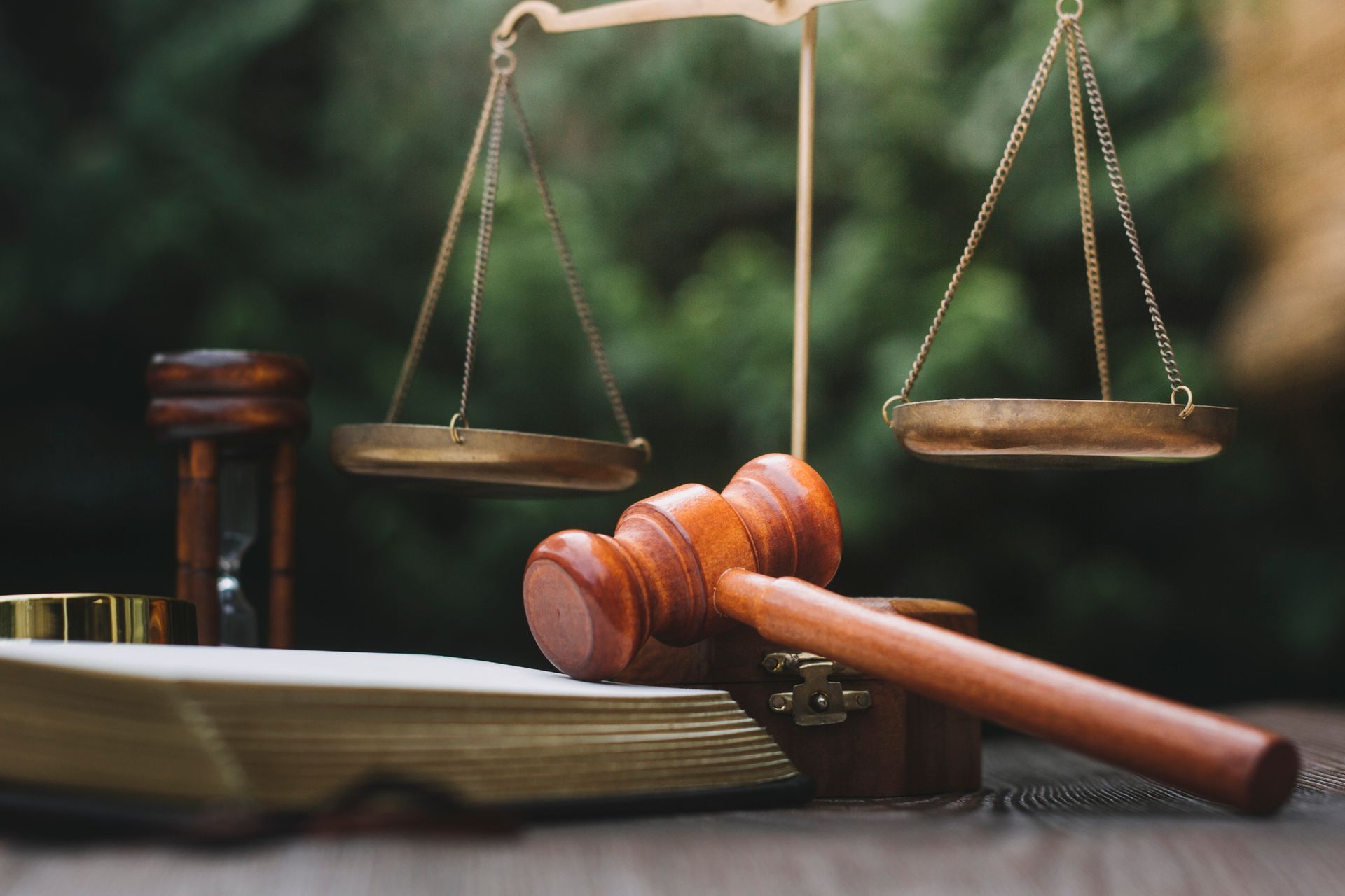 A wooden gavel is sitting on top of a book next to a scale of justice.