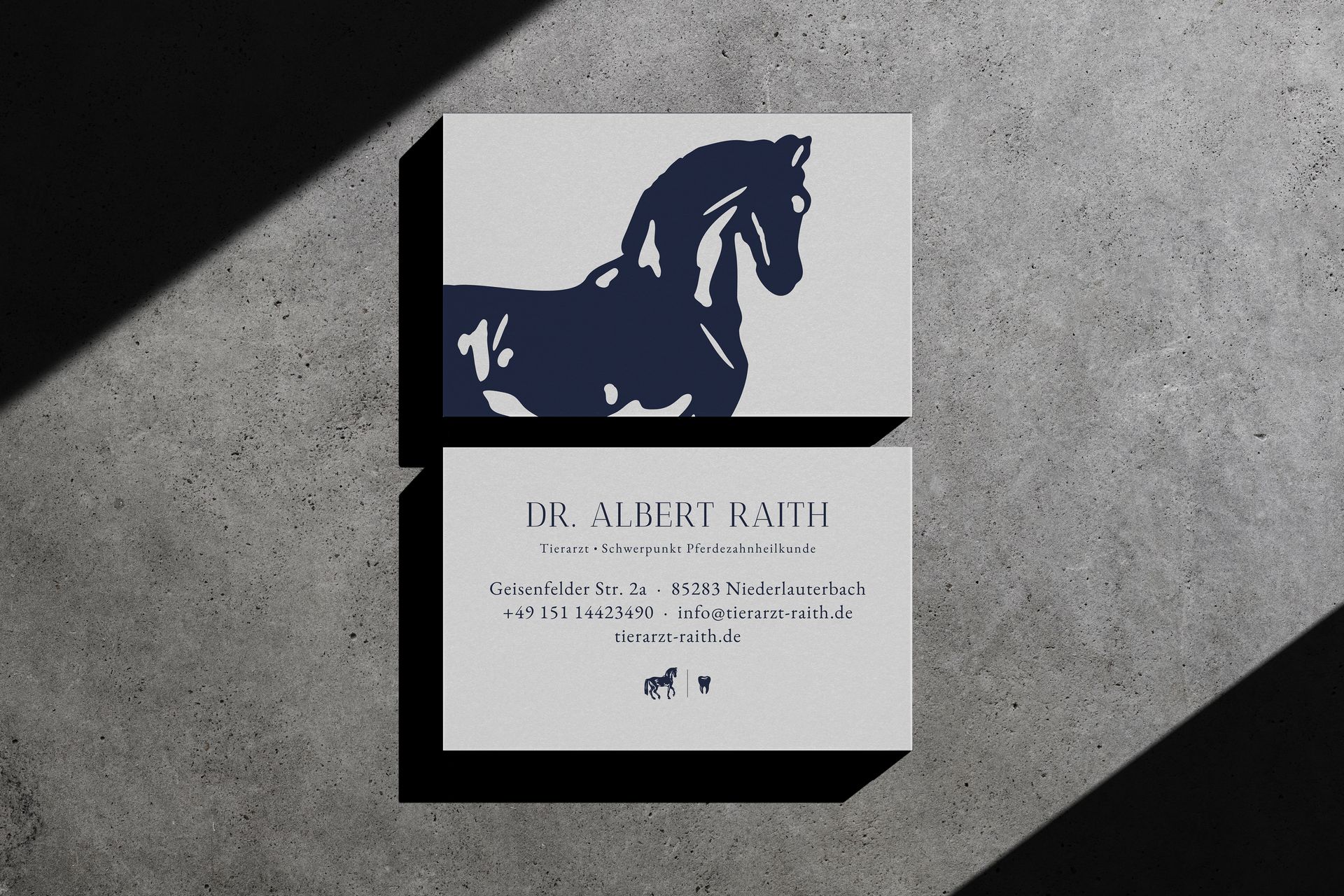 Zwei Visitenkarten auf Betonhintergrund; die obere Karte zeigt die Silhouette eines Pferdes. Die untere Karte enthält Text.