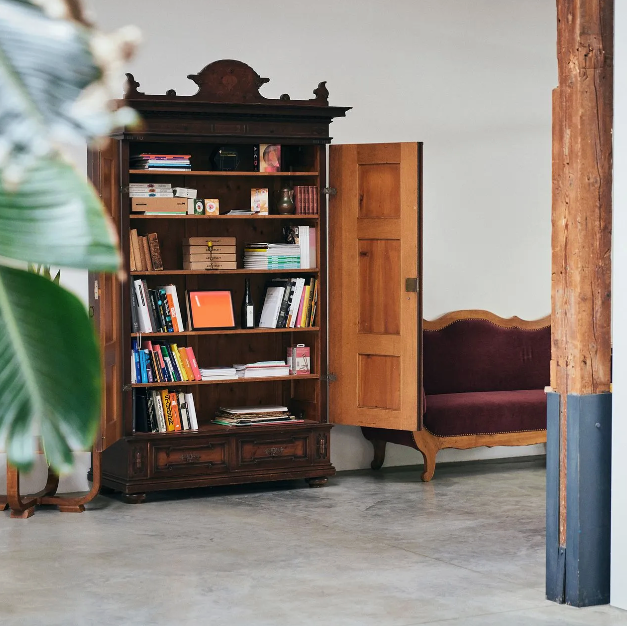 Ein hölzernes Bücherregal mit offener Tür, gefüllt mit Büchern, kleinen Schachteln und Dekorationsgegenständen.