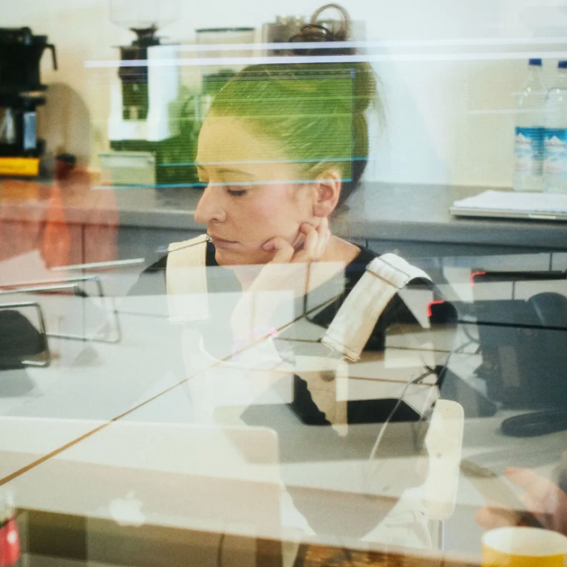 Frau in gestreiftem Top an einem Tresen, konzentriert, mit sichtbaren Spiegelungen des Café-Interieurs.