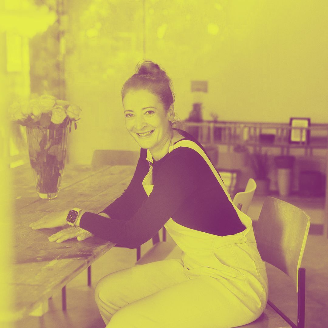 Eine Frau lächelt, während sie an einem Tisch in der Nähe eines Fensters sitzt. 