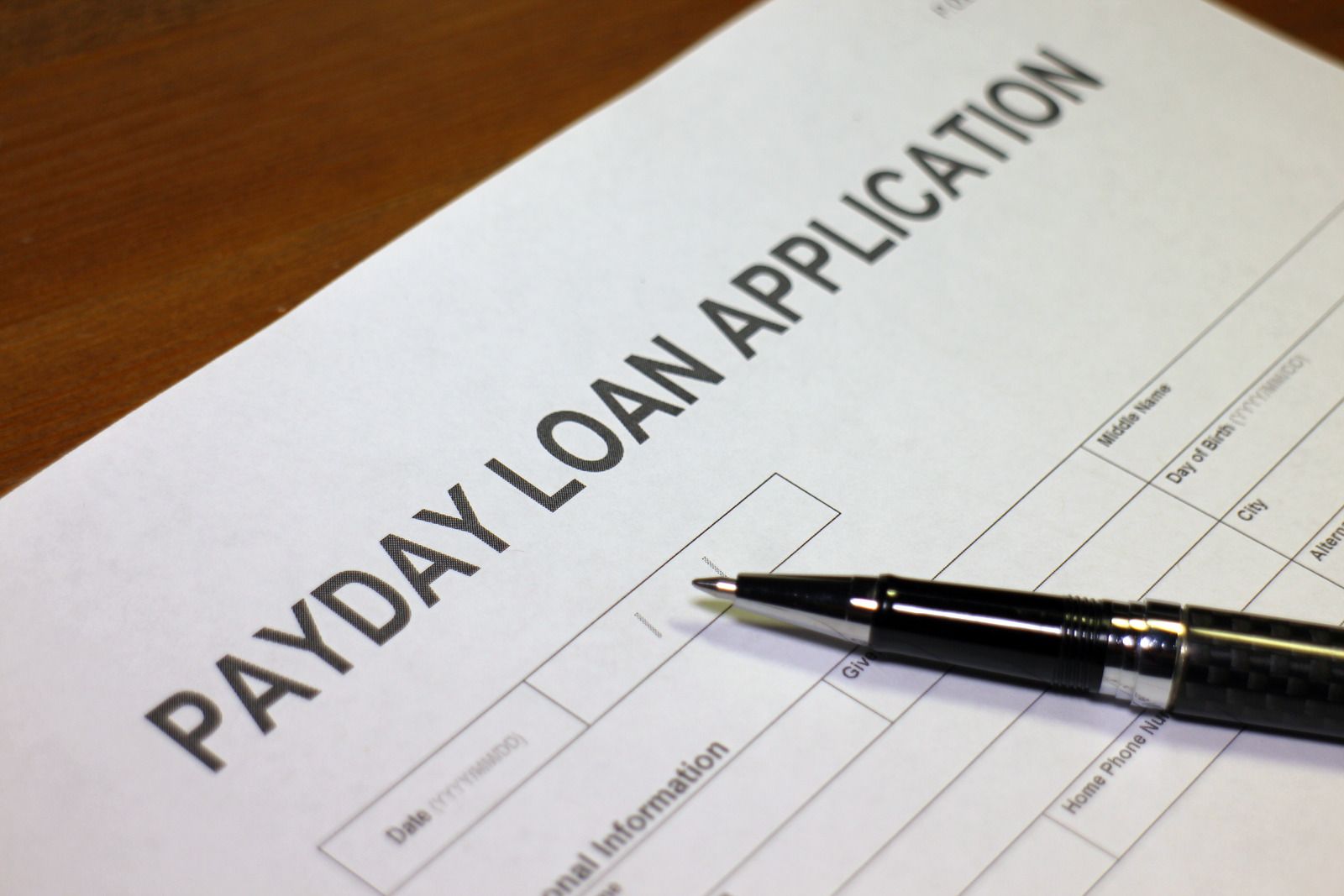 Payday loan application form with a pen resting on it, on a wooden surface.