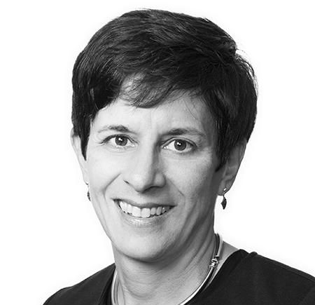 Woman with short dark hair, smiling, wearing a dark top, and silver necklace.