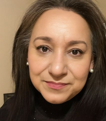 Woman with long dark hair, wearing pearl earrings, looking towards the camera, soft smile.