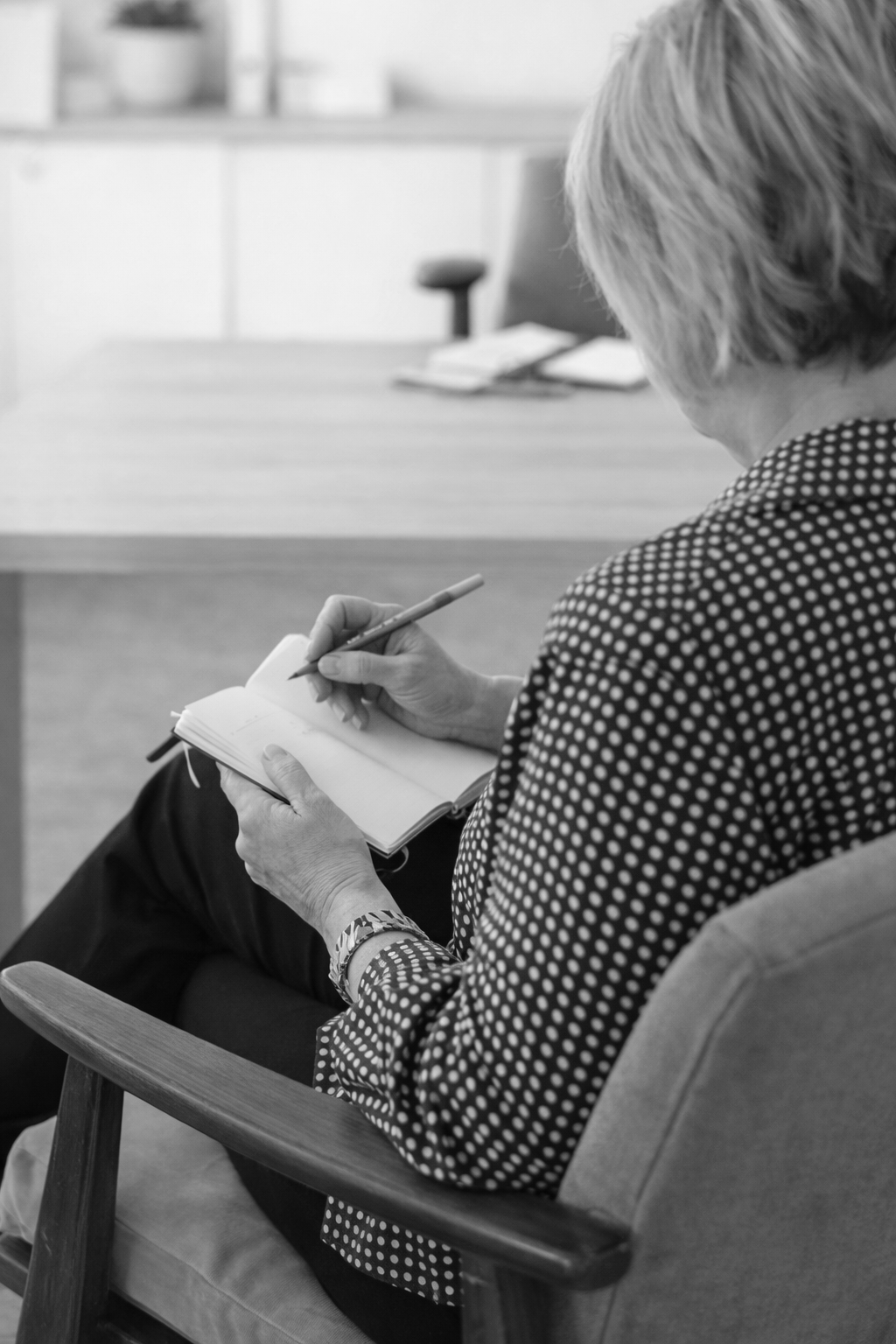 Woman in checkered shirt, smiling broadly, hands clasped, indoors.