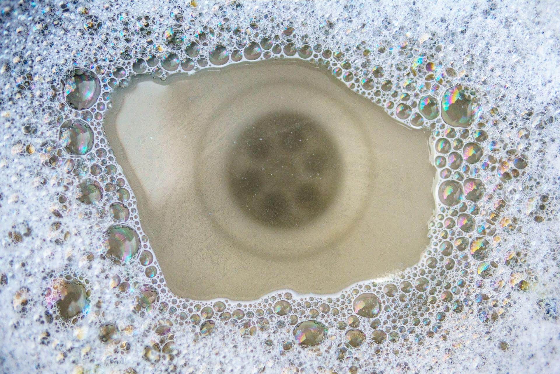 Uno scarico del lavandino pieno di acqua saponata e bolle.