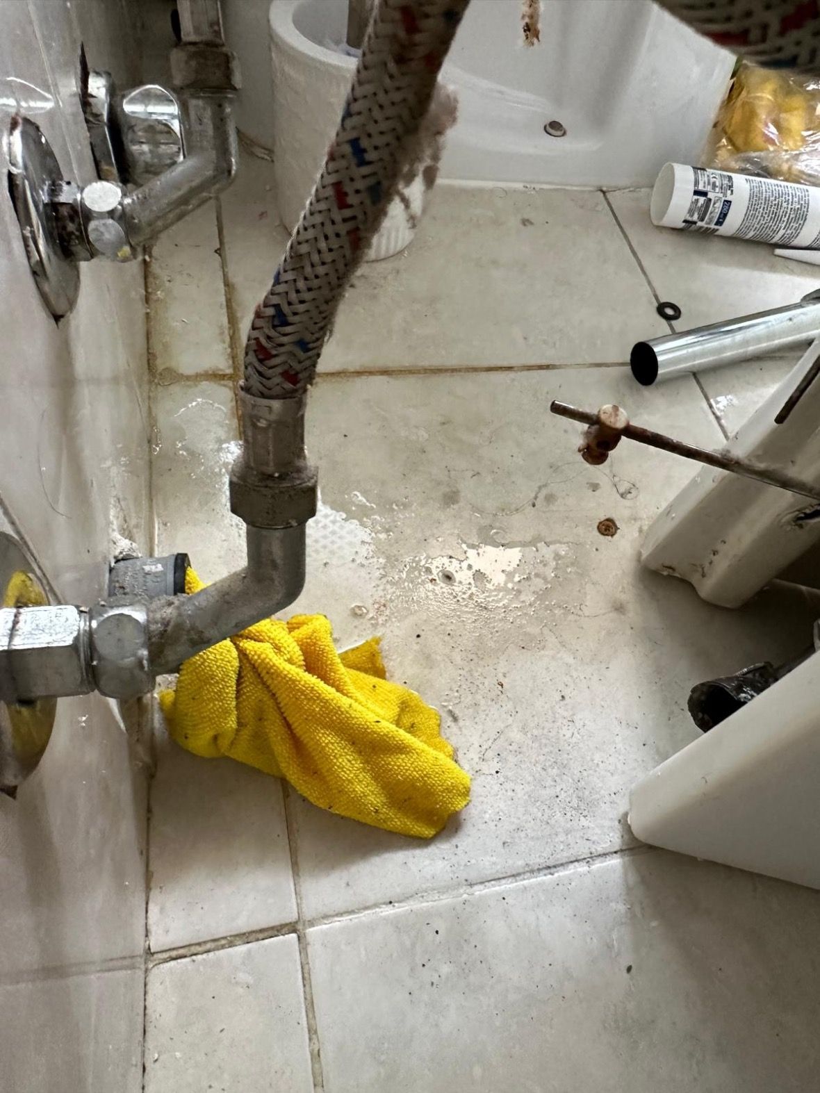Un asciugamano giallo è steso sul pavimento accanto a un tubo in un bagno.