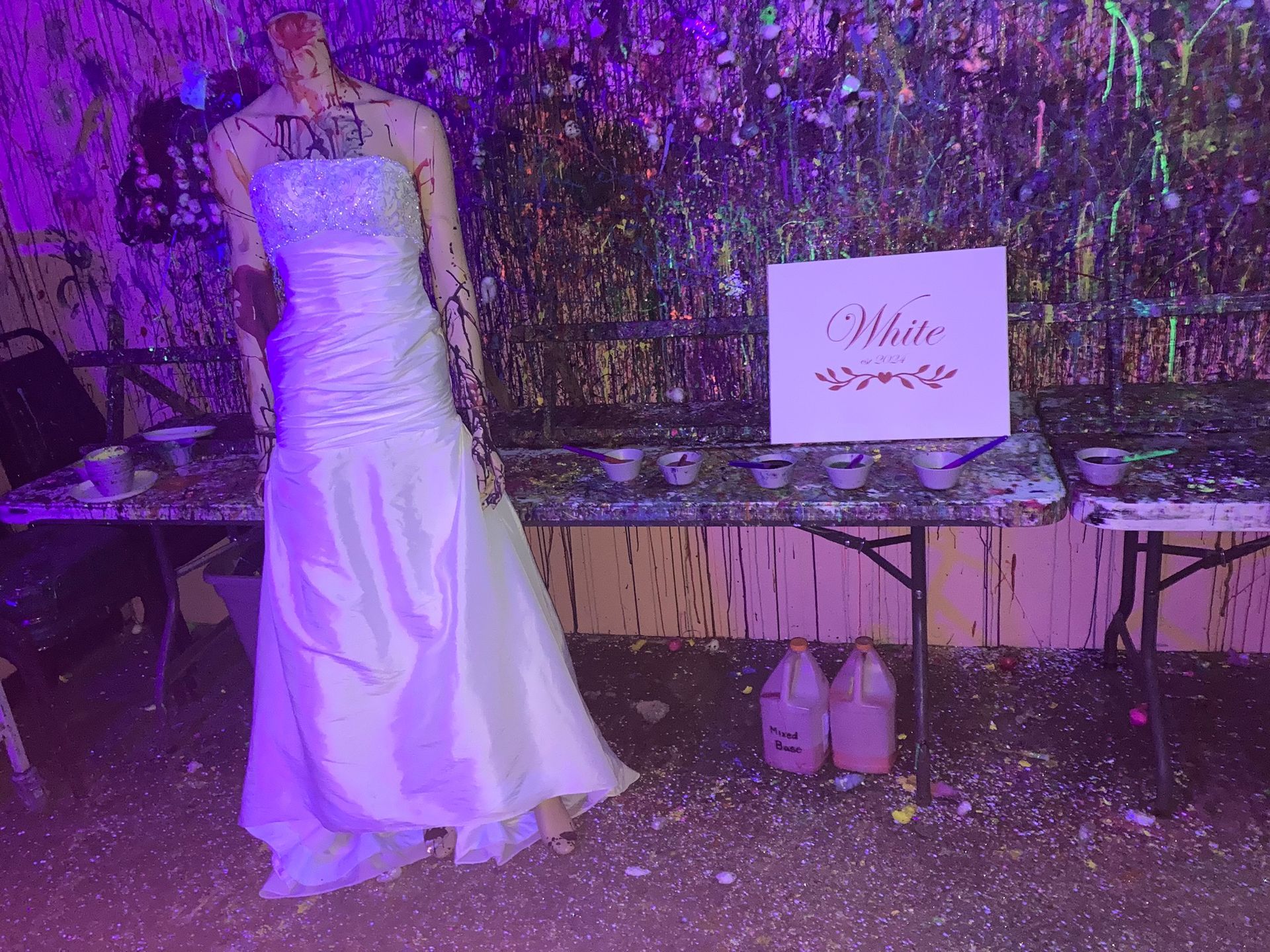 A mannequin in a wedding dress is standing in front of a table covered in paint.
