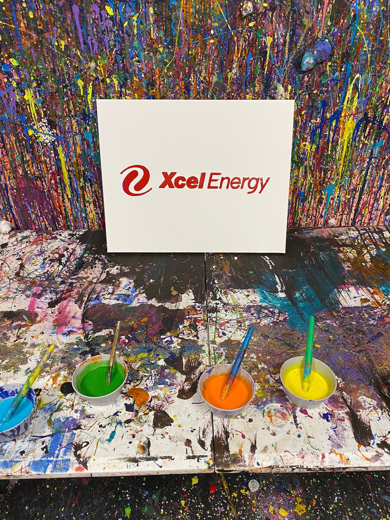 A sign that says xcel energy is sitting on a table next to a painting.