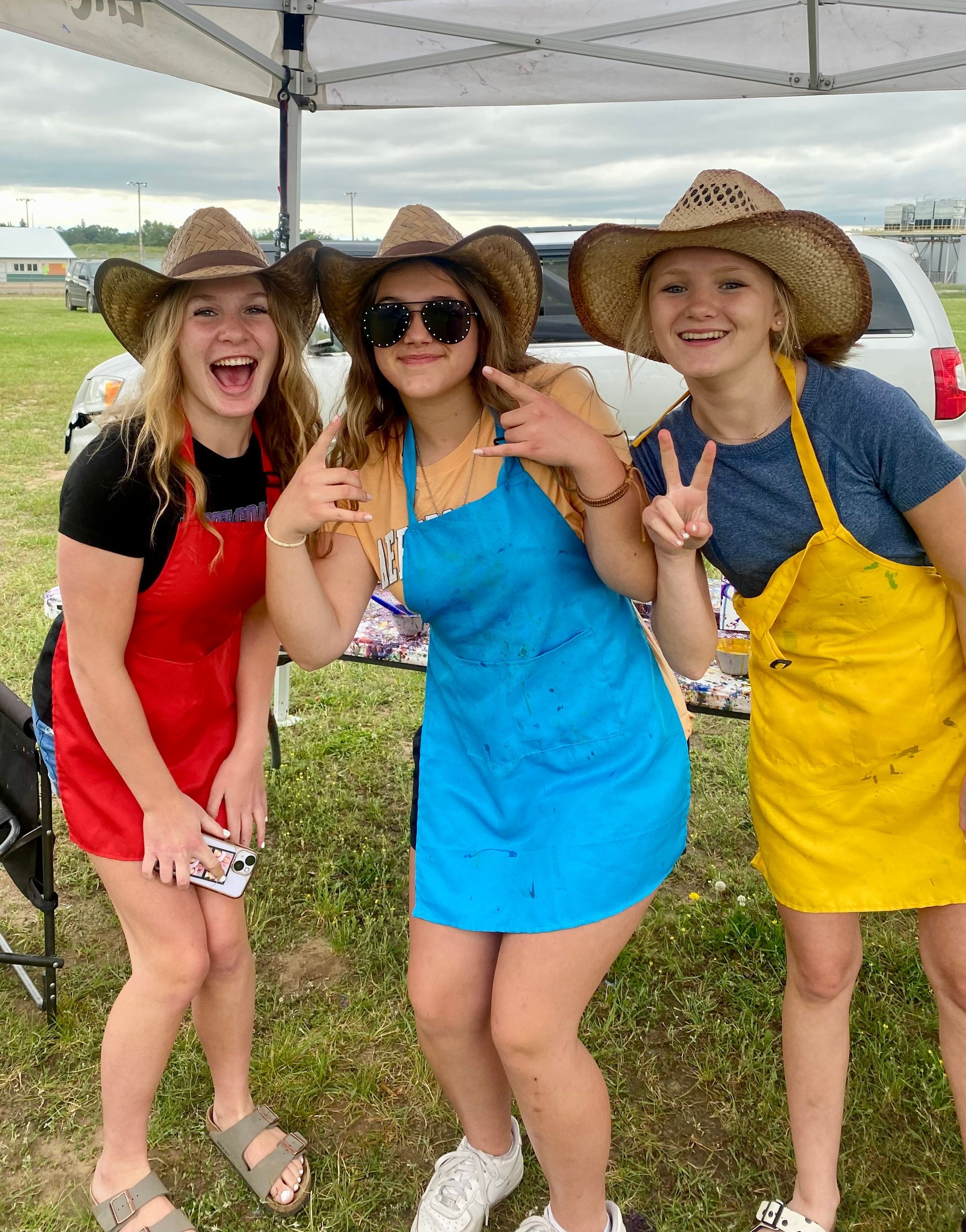 Three girls wearing cowboy hats and aprons are posing for a picture.