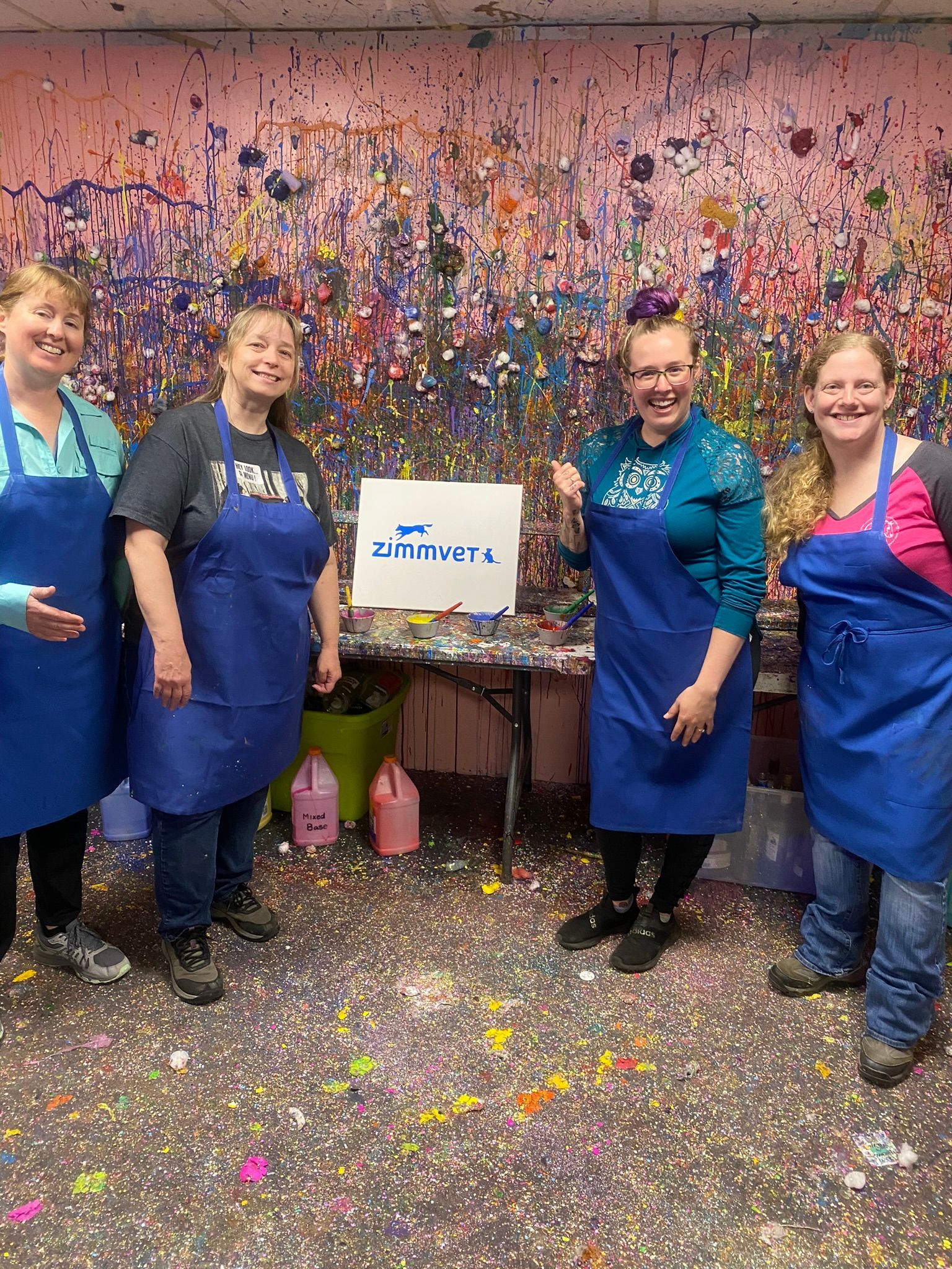 A group of women in blue aprons are standing in front of a wall covered in paint.