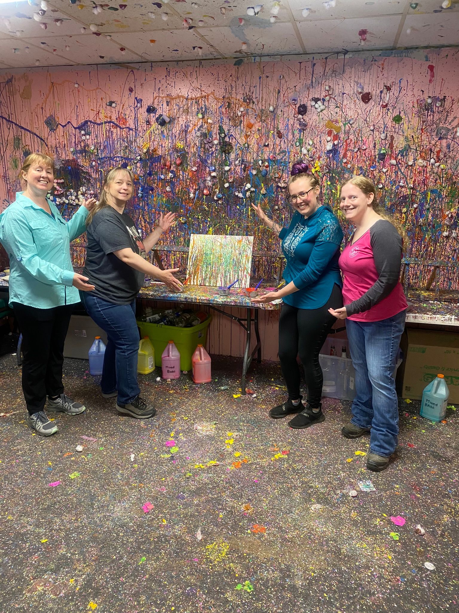 A group of women are standing in front of a painting on a table.