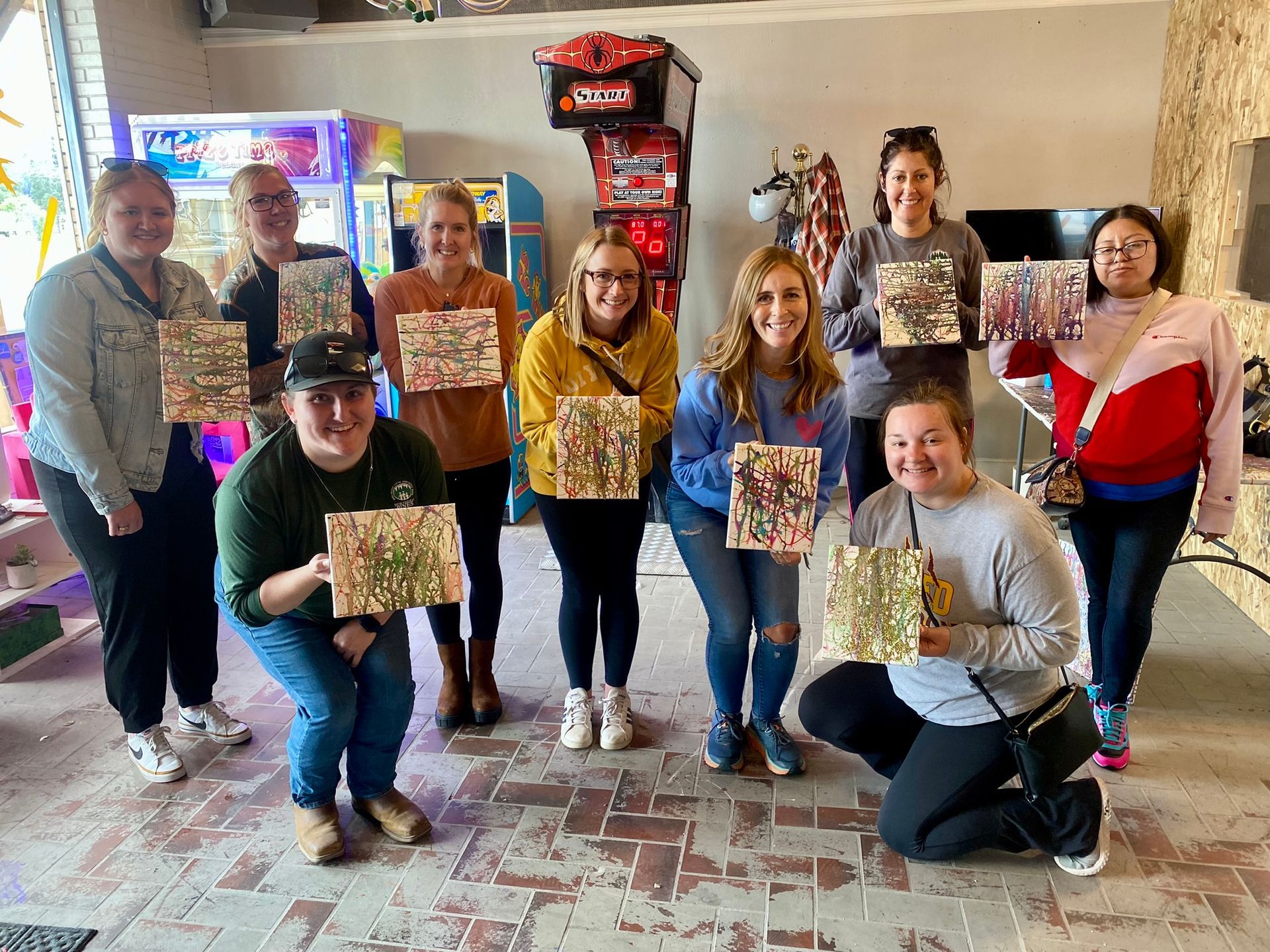 A group of people are posing for a picture while holding paintings in a room.