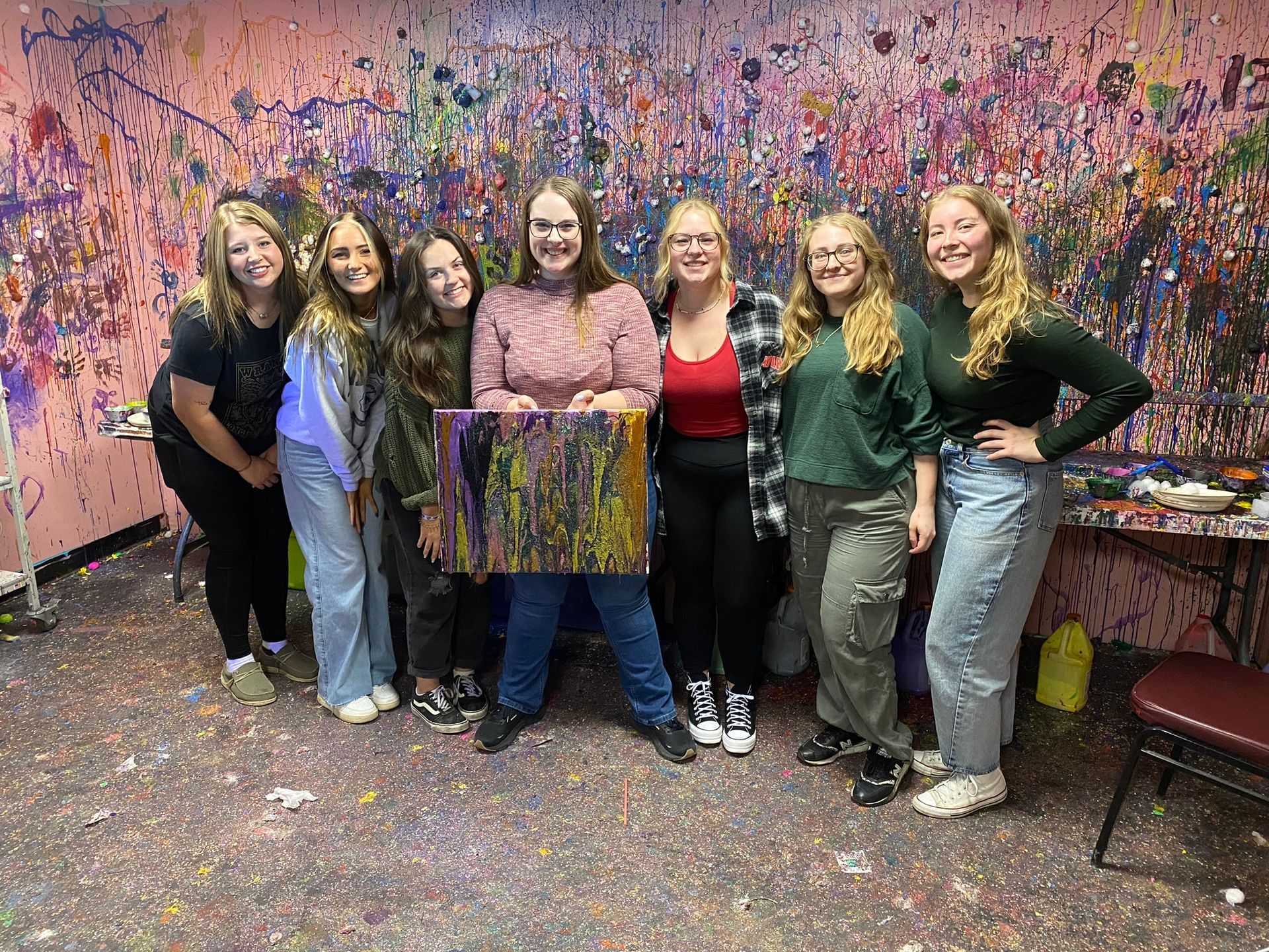A group of women are posing for a picture in front of a wall covered in paint.