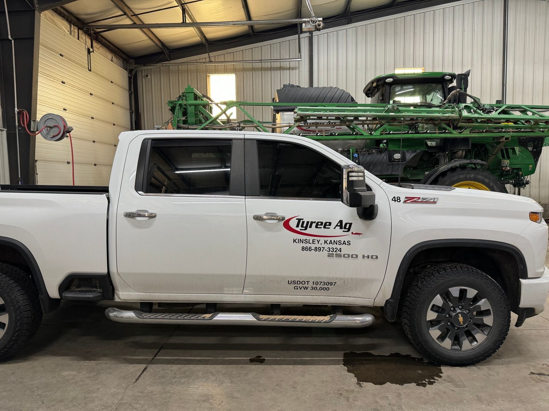 A white truck is parked in a garage next to a green tractor.