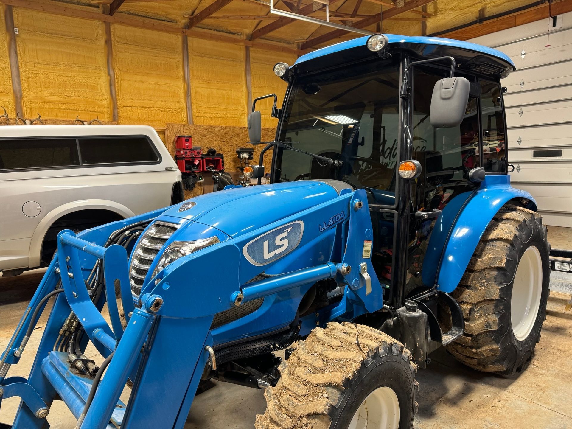 A blue tractor is parked in a garage next to a white truck.
