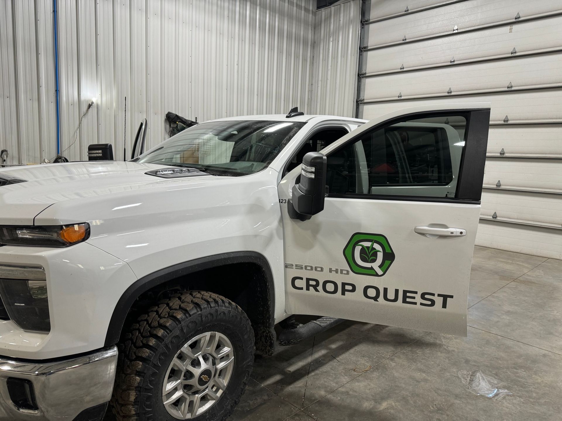 A white truck with crop quest written on the side is parked in a garage.