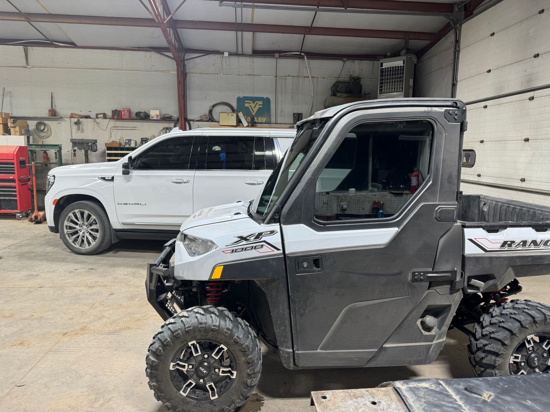 A polaris ranger is parked in a garage next to a white suv.