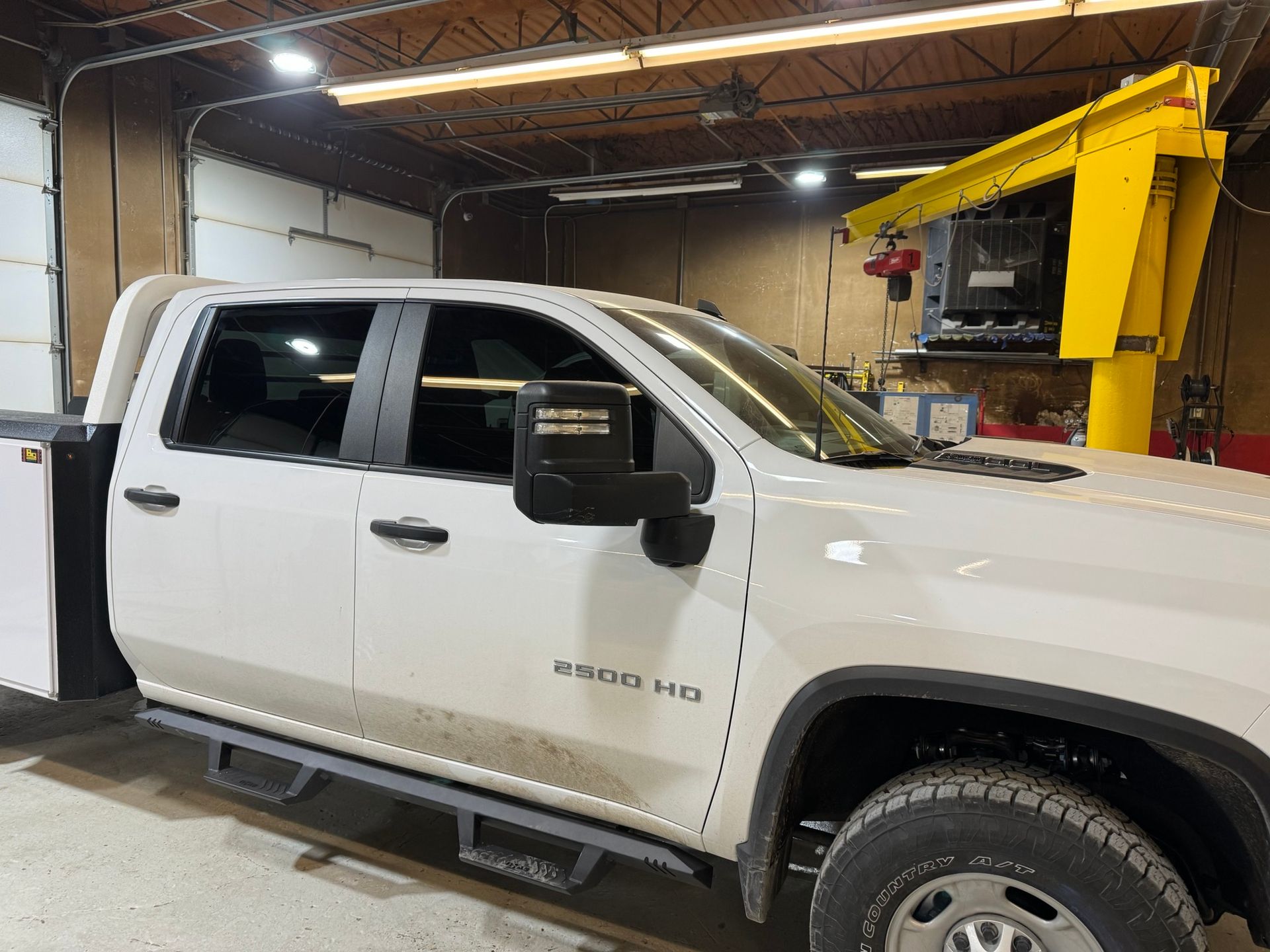 A white truck is parked in a garage next to a yellow crane.