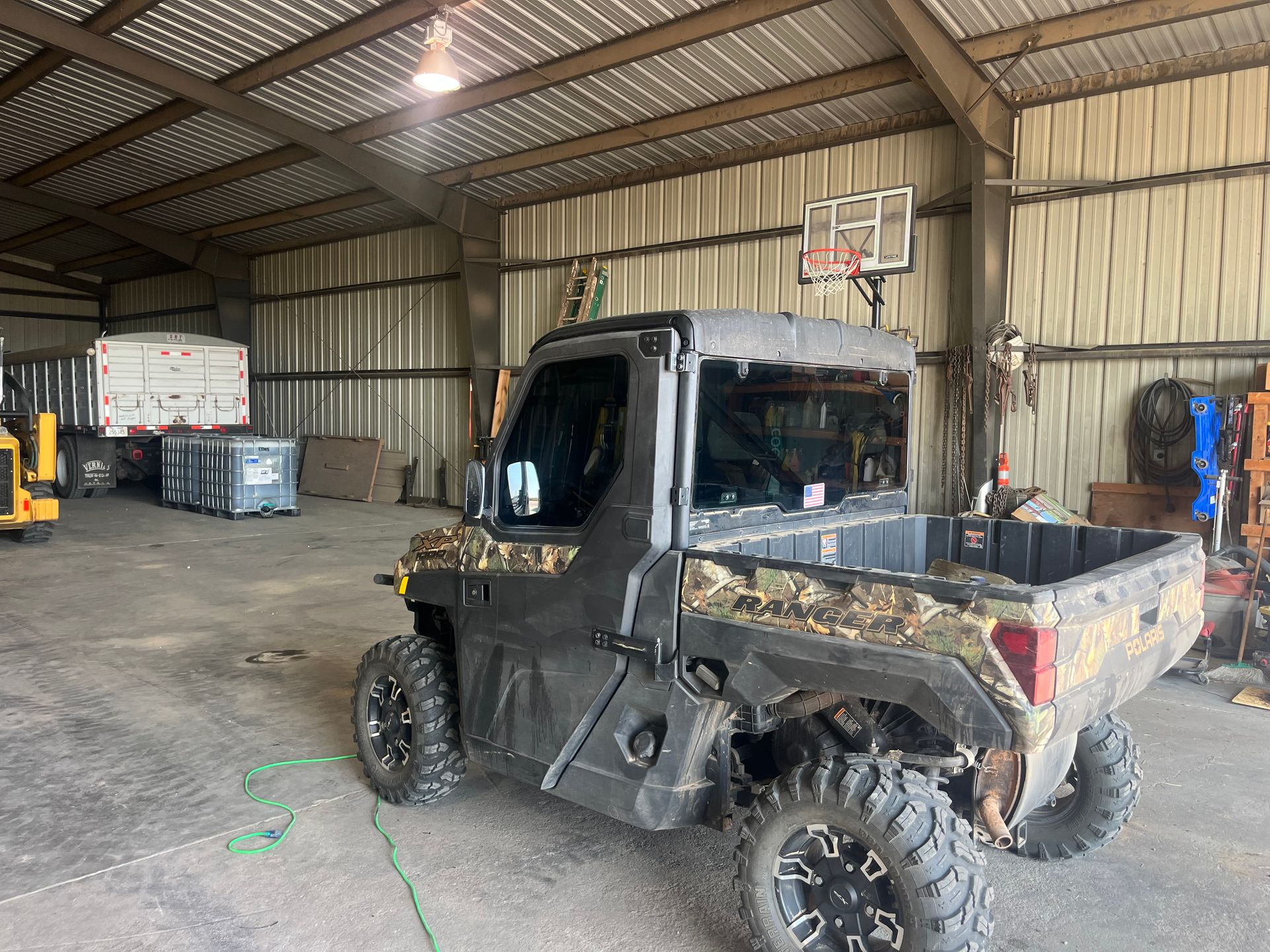 A utility vehicle is parked in a warehouse next to a basketball hoop.