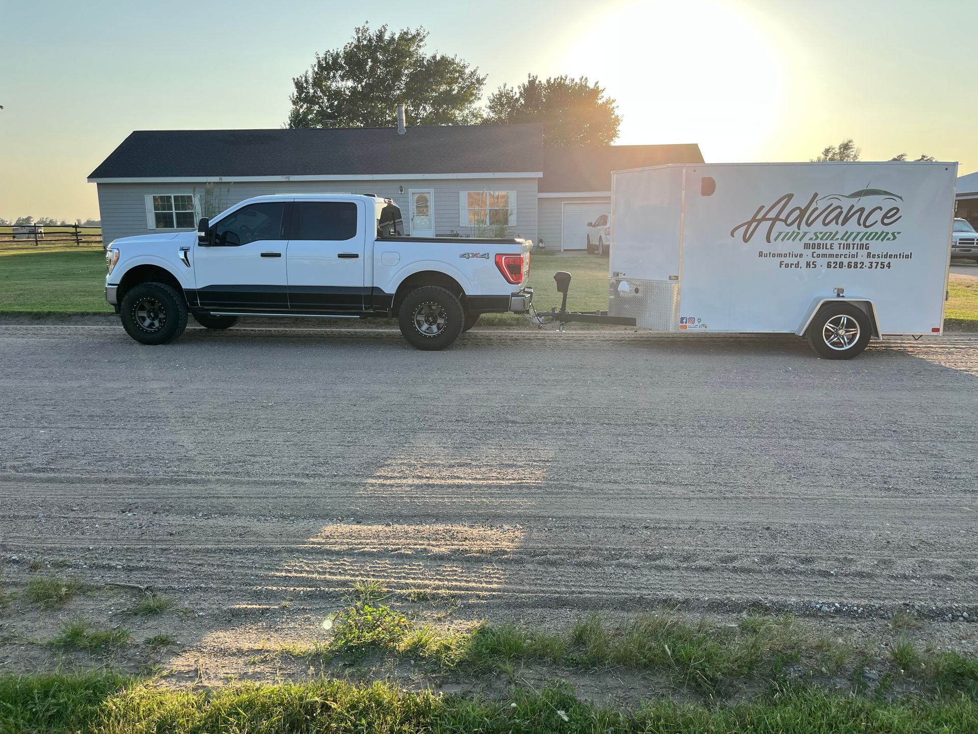 A white truck with a trailer attached to it is parked in front of a house.