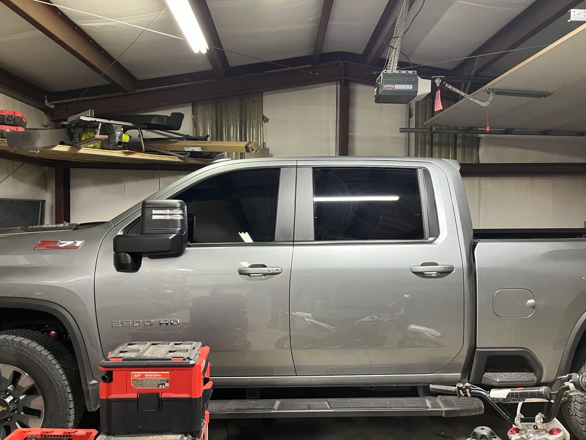 A silver truck is parked in a garage with a garage door open.