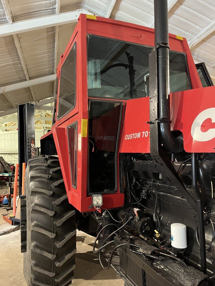 A red tractor is parked in a warehouse with the door open.