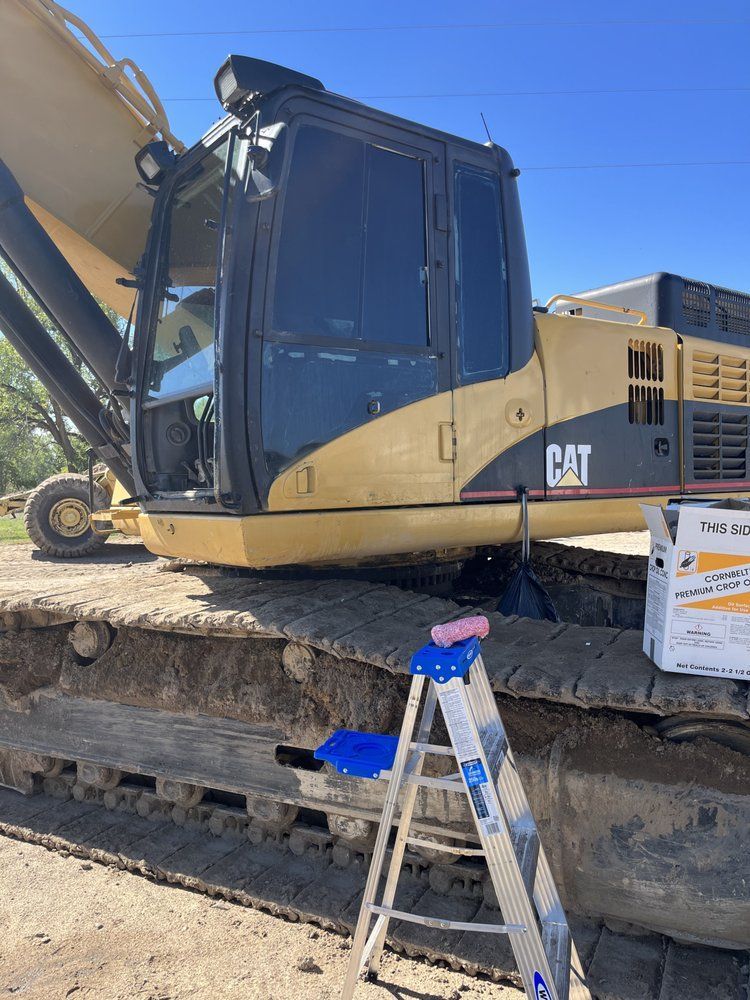 A cat excavator is parked next to a blue ladder.