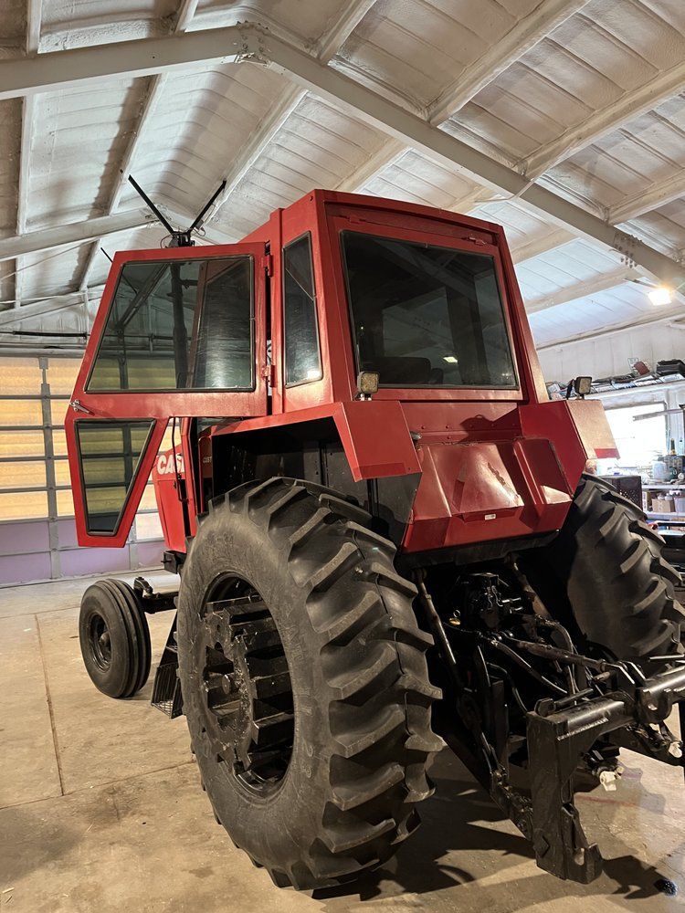A red tractor is parked in a garage with its doors open.