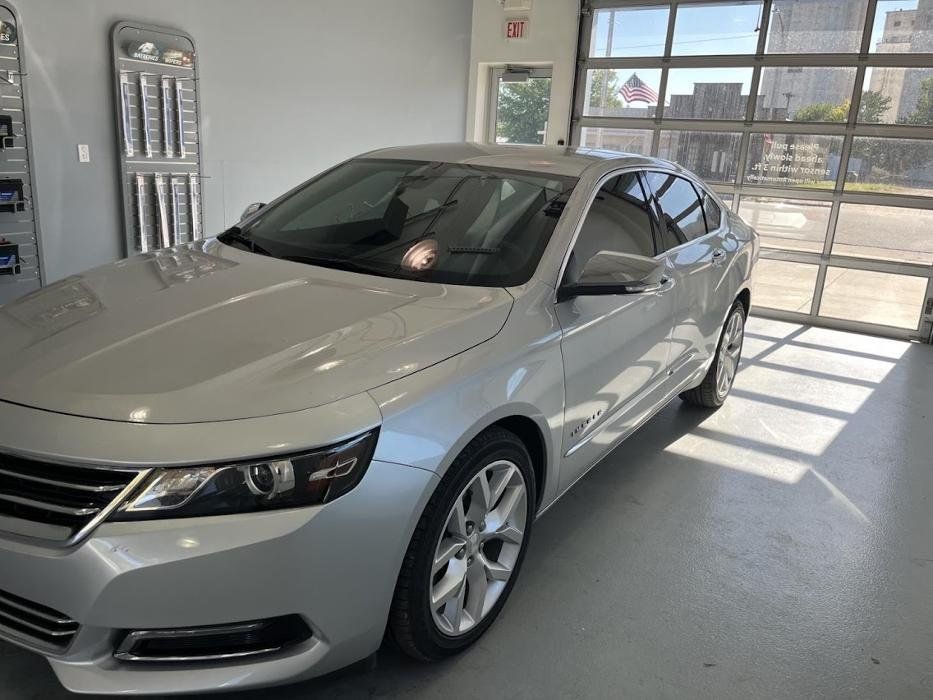 A silver car is parked in a garage with a glass door.