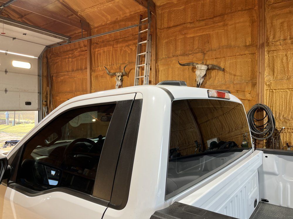 A white truck is parked in a garage with two deer skulls on the wall.