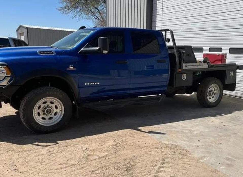 A blue truck with a flat bed is parked in front of a garage door.
