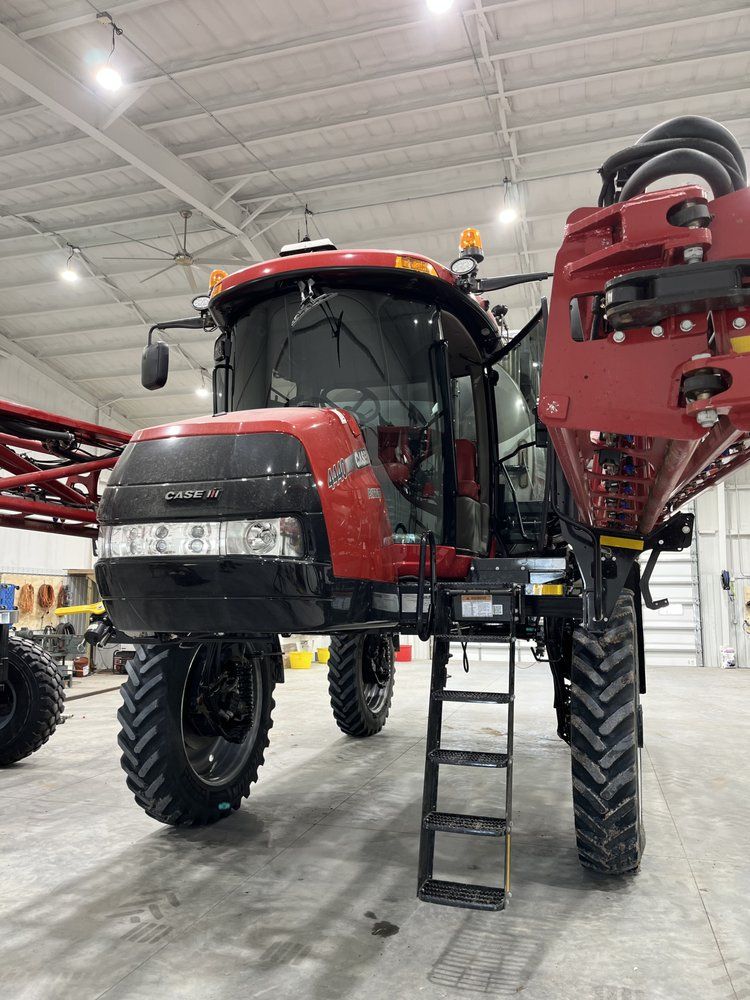 A red and black tractor is parked in a warehouse with a ladder attached to it.