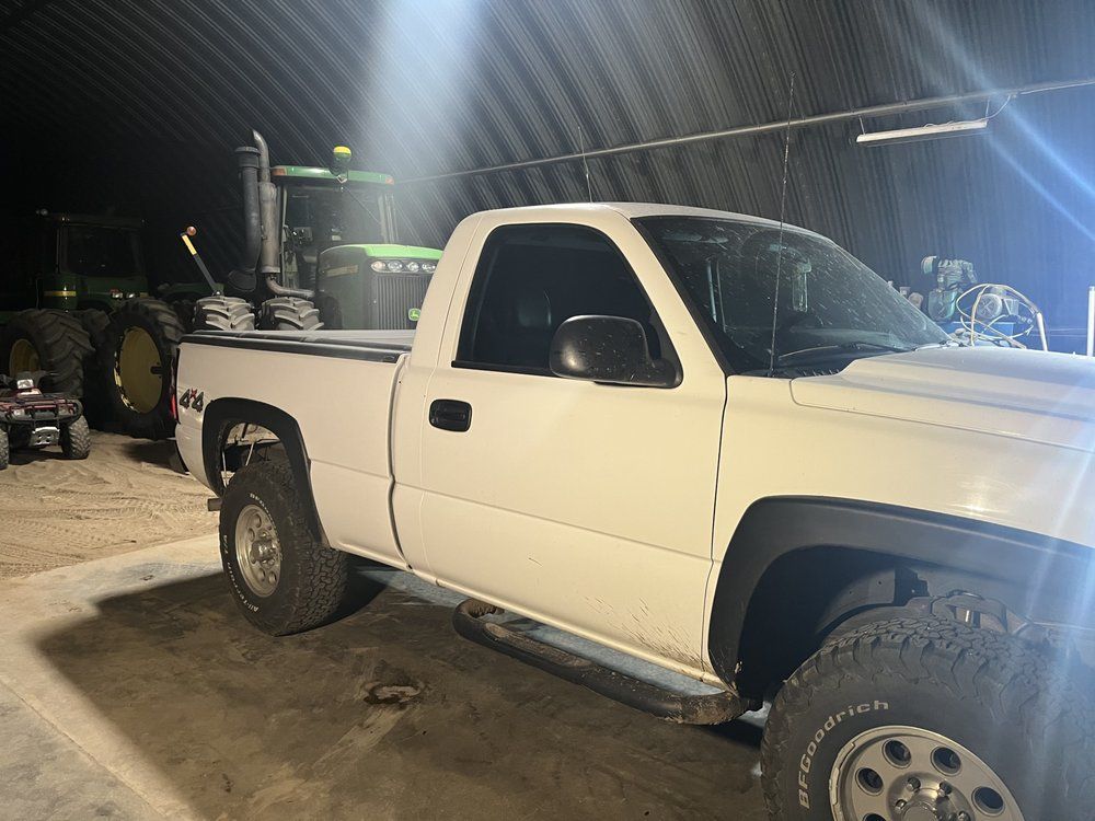 A white truck is parked in a garage next to a green tractor.