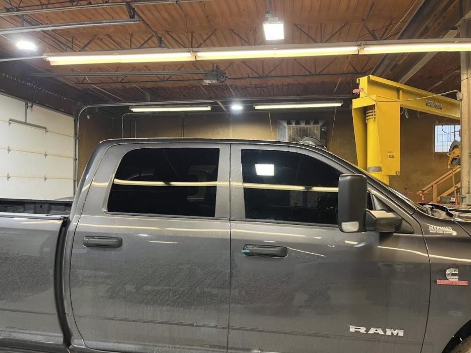 A gray ram truck is parked in a garage with a yellow crane in the background.