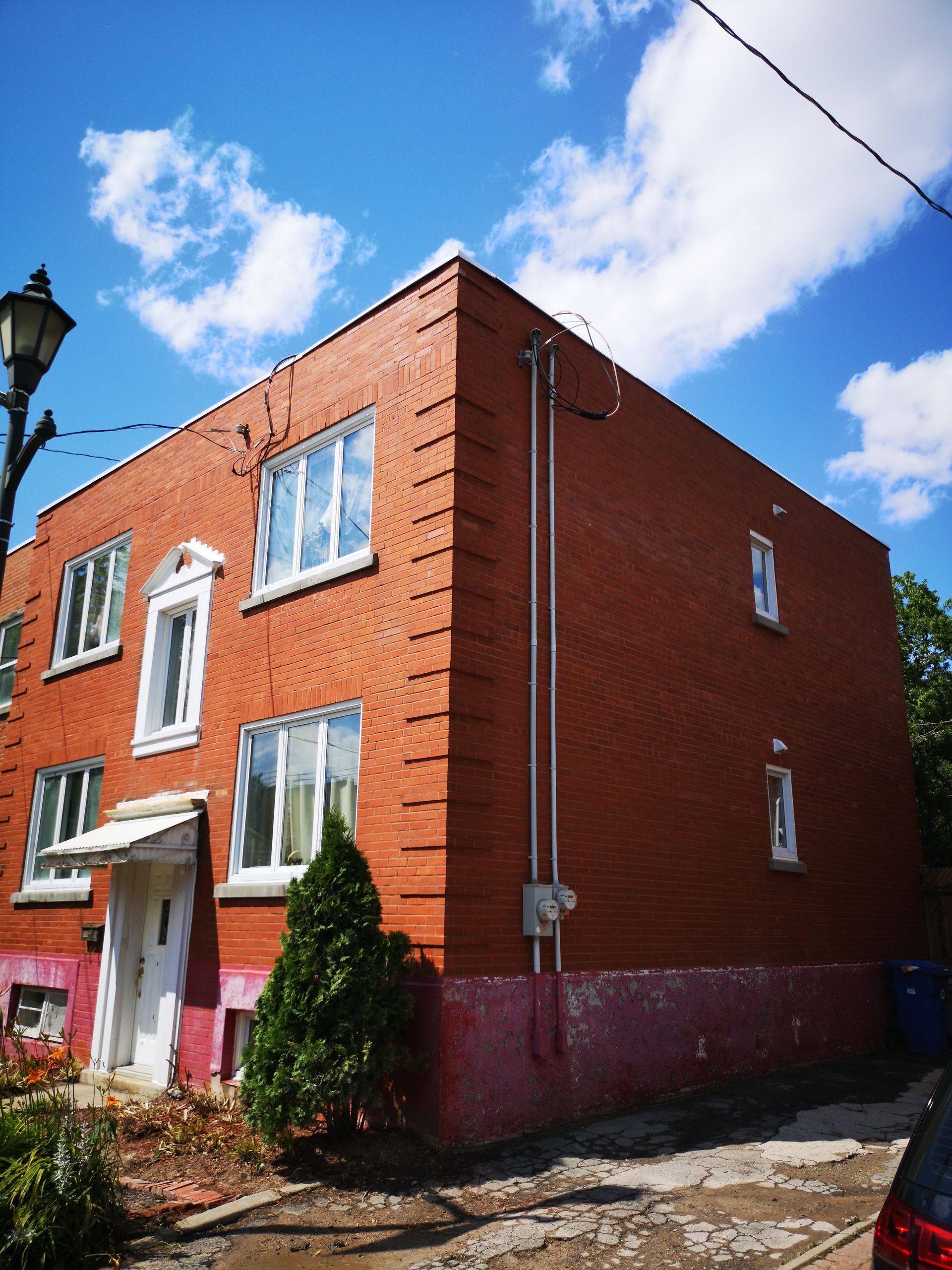 Bâtiment en briques avec des fenêtres à encadrement blanc, une porte blanche et un petit arbre vert.