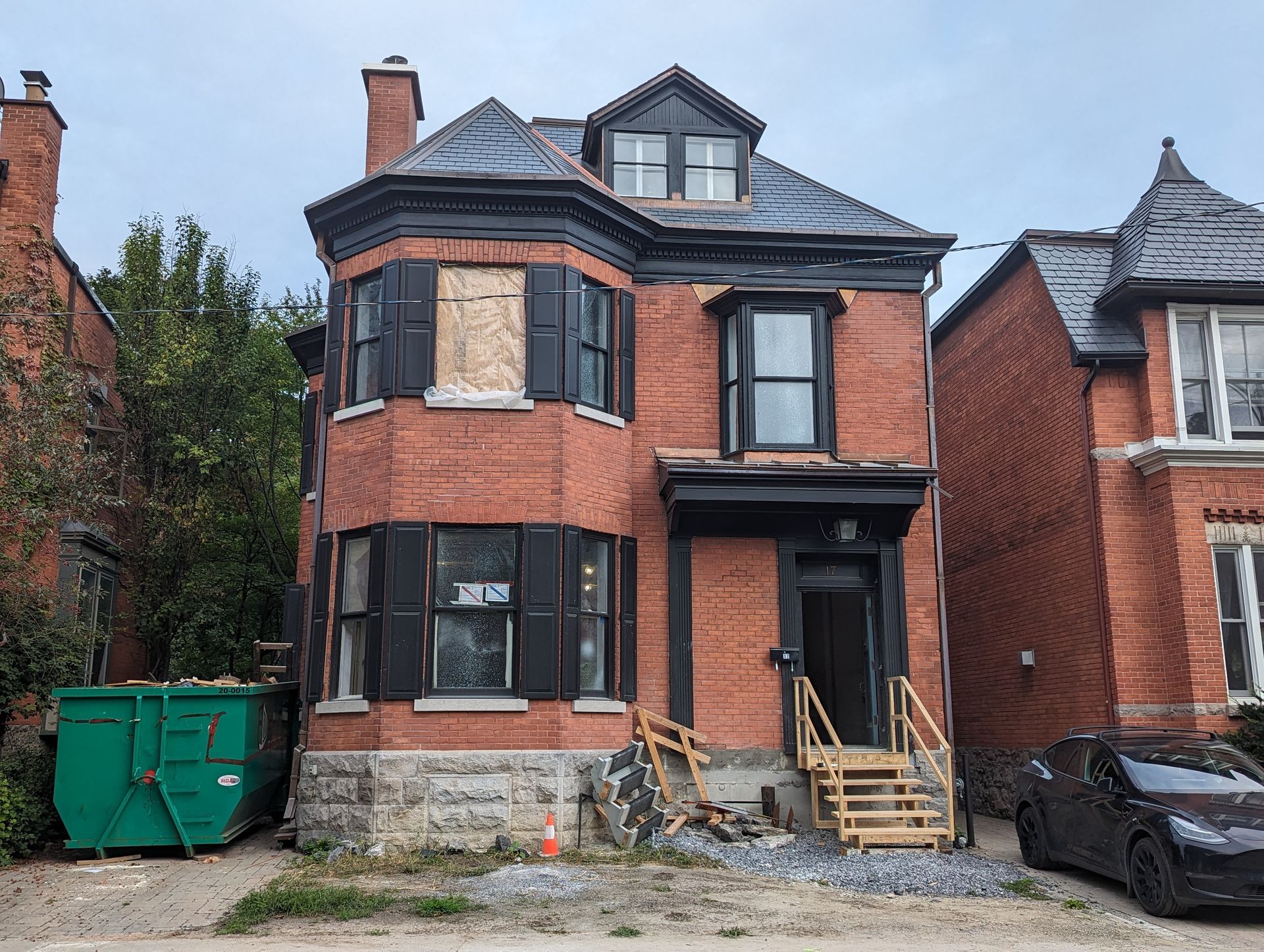 Une maison en brique avec des volets noirs et une voiture noire garée devant.