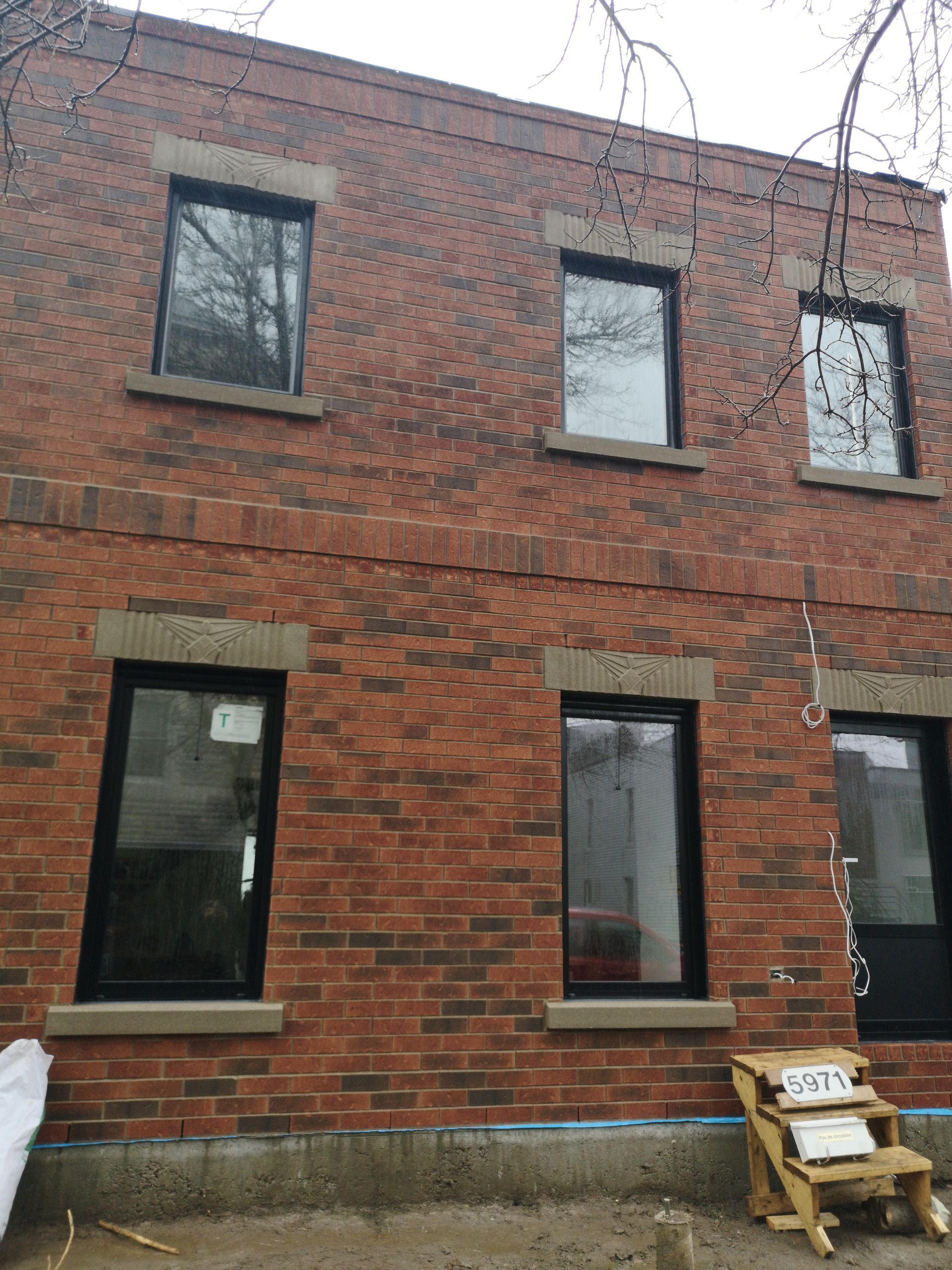 Un bâtiment en brique avec des fenêtres noires et une chaise en bois devant.