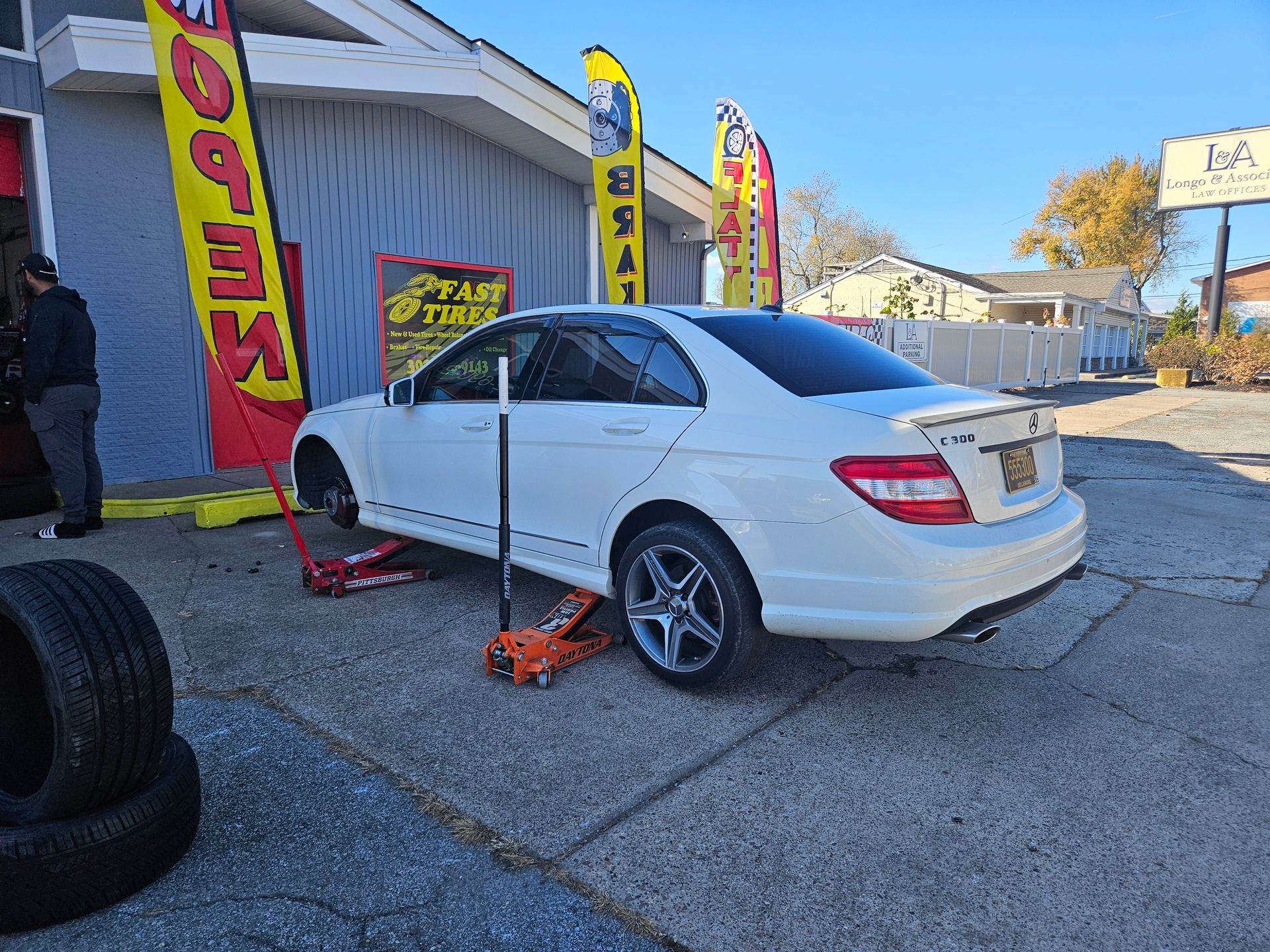 A white car is sitting on a jack in front of a building.