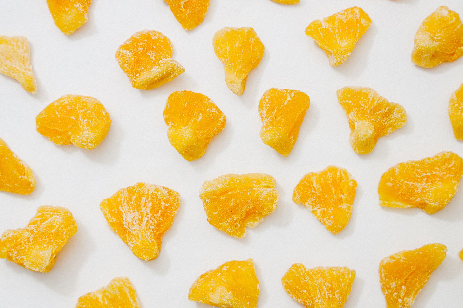 A scattered arrangement of bright orange, crystalline dried fruit pieces on a solid white background.