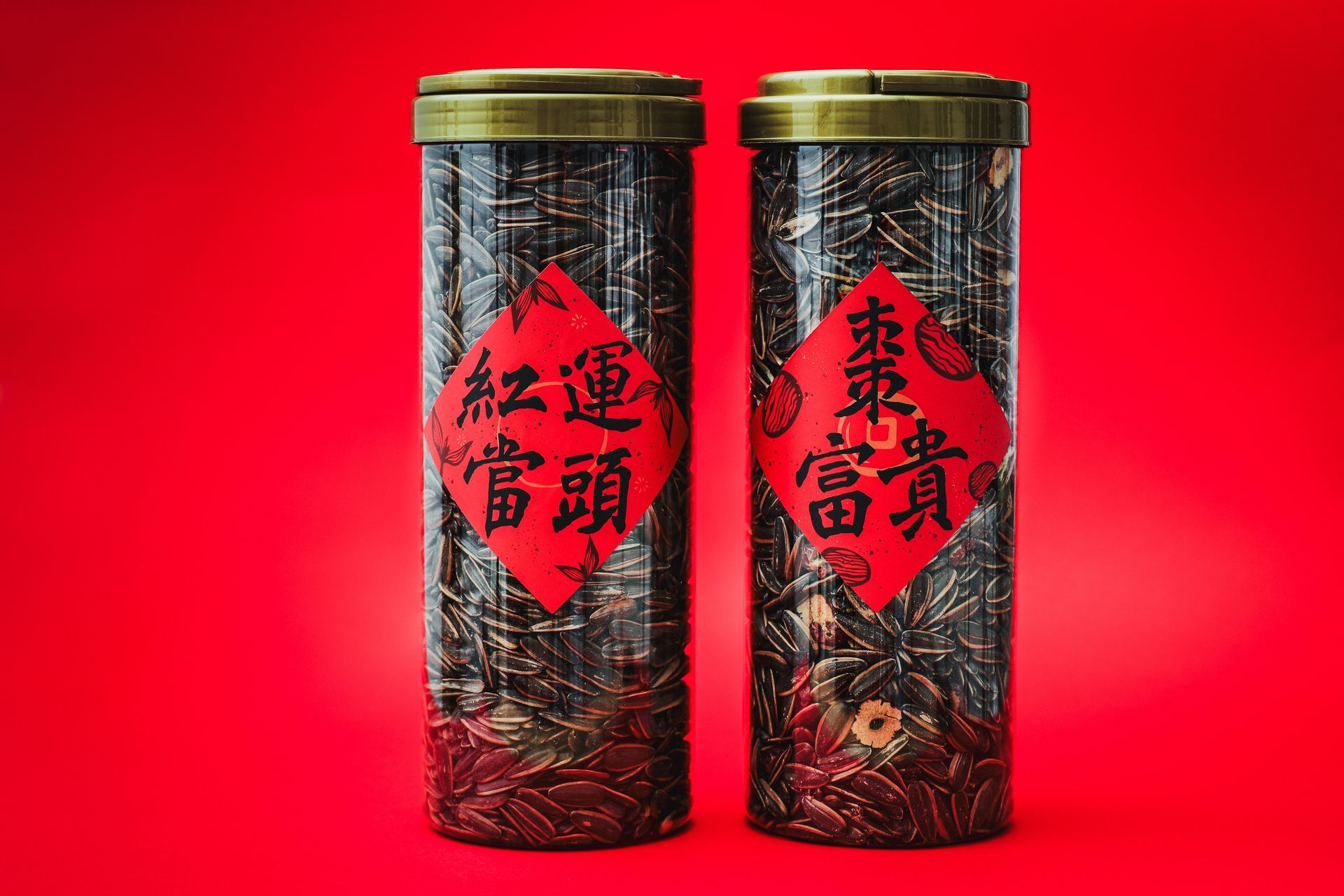 A wooden bowl filled with sunflower seeds, surrounded by scattered seeds on a dark stone surface with a red cloth backdrop.