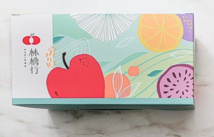 A rectangular box with a fruit-themed illustration featuring a large red apple, citrus, and a purple dragon fruit graphic.