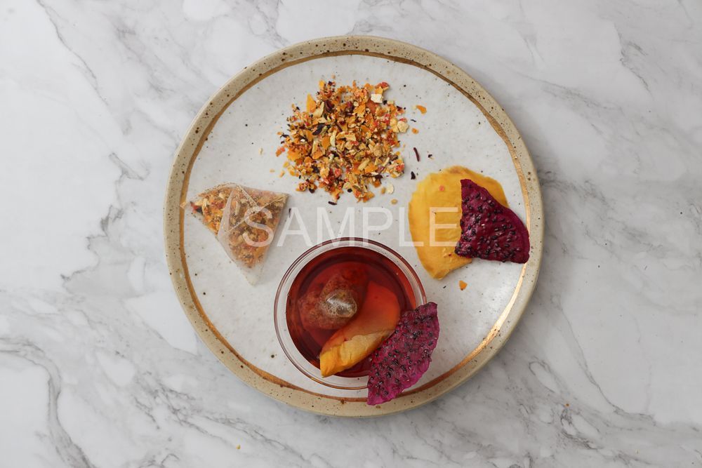 A top-down view of a speckled ceramic plate with a small bowl of fruit-infused water, dried fruit, and a garnish mix.