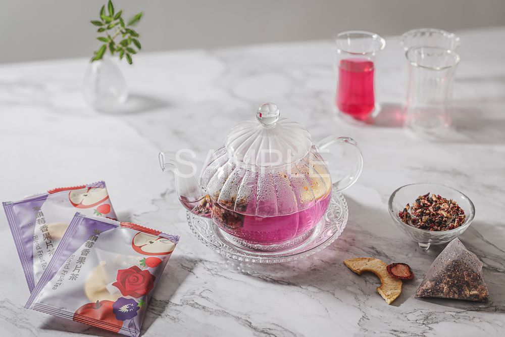 A tea sachet, a pile of loose herbal tea, and dried fruit slices arranged on a plate with a small bowl of brewed tea.