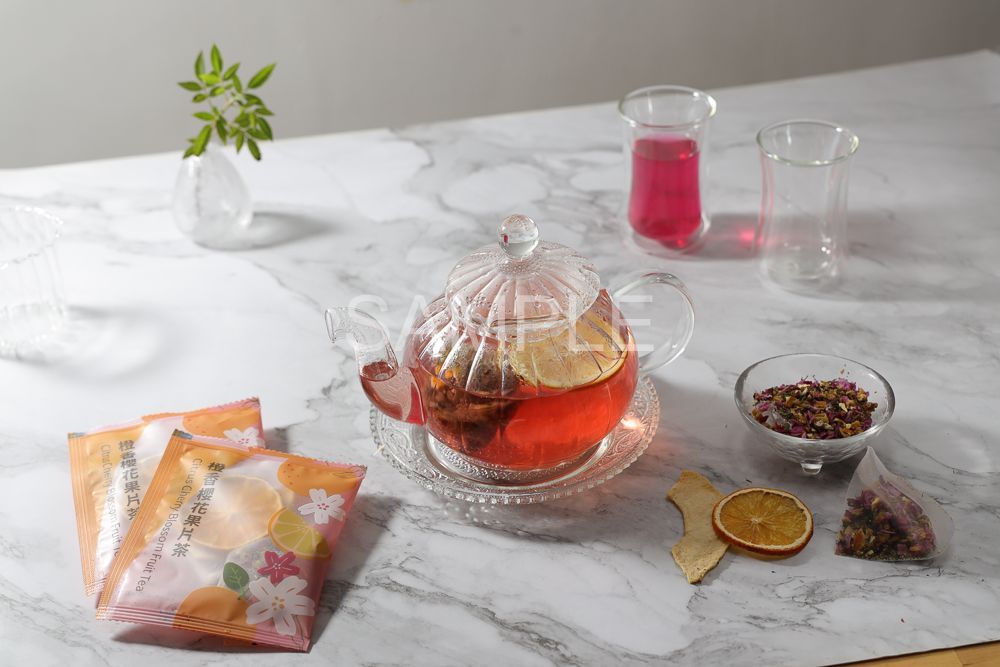 A top-down view of a ceramic plate with loose tea, tea bags, a cup of steeped tea with orange slices, and chips on marble.
